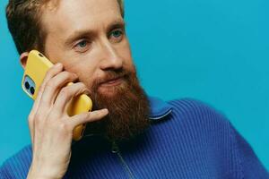 retrato de un hombre con un teléfono en su manos lo hace mirando a eso y hablando en el teléfono, en un azul antecedentes. comunicado en línea social medios de comunicación, estilo de vida foto