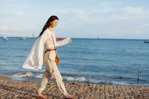 un mujer contento en el Dom caminando en el playa con su brazos untado fuera en contra el fondo de el Oceano sonrisa, volador cabello, bronceado piel, relajación, viaje a el Oceano y libertad, puesta de sol ligero bali foto