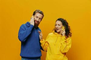 Woman and man cheerful couple with phones in hand talking on cell phone crooked smile cheerful, on yellow background. The concept of real family relationships, talking on the phone, work online. photo