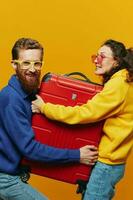 mujer y hombre sonriente, maletas en mano con amarillo y rojo maleta sonriente alegremente y torcido, amarillo fondo, yendo en un viaje, familia vacaciones viaje, recién casados. foto