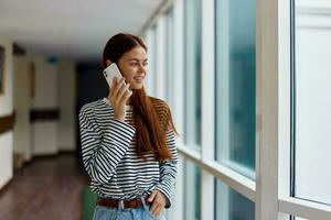 A woman with red hair with a phone in her hands talks and laughs while looking out the window at the city photo