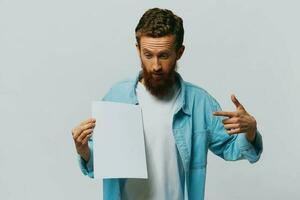 Portrait of an adult male on a gray background with a white sheet of paper in his hands for your design and text, layout, copy space, space for text, finger pointing photo