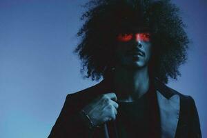 Fashion portrait of a man with curly hair on a blue background with a red stripe of light, multicolored light, trendy, modern concept. photo