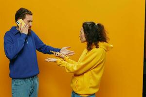 Woman man cheerful couple with phones in hand social networking and communication crooked smile fun and fight, in yellow background. The concept of real family relationships, freelancers, work online. photo