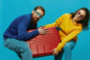 Woman and man smile suitcases in hand with yellow and red suitcase smile fun, on blue background, packing for a trip, family vacation trip. photo
