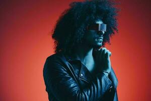 Portrait of fashion man with curly hair on red background with stylish glasses, multicultural, colored light, black leather jacket trend, modern concept. photo