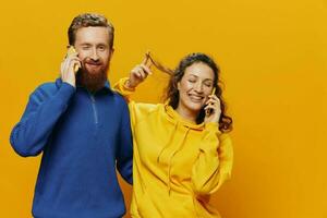 Woman and man cheerful couple with phones in hand talking on cell phone crooked smile cheerful, on yellow background. The concept of real family relationships, talking on the phone, work online. photo