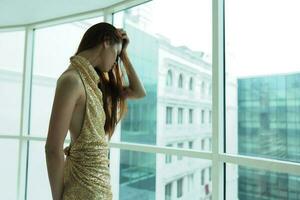 Woman in gold sequined dress standing by the window posing in a stylish look with long hair, designer dress with open back, party look photo