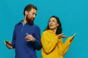 mujer y hombre alegre Pareja con Los telefonos en su manos torcido sonrisa alegre, en azul antecedentes. el concepto de real familia relaciones, hablando en el teléfono, trabajo en línea. foto