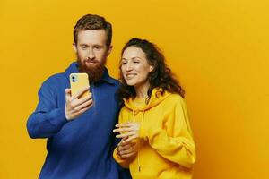 Man and woman couple smiling merrily with phone in hand social media viewing photos and videos, on yellow background, symbols signs and hand gestures, family freelancers.