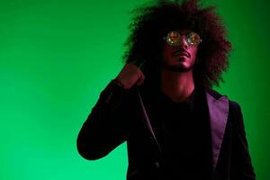 Fashion portrait of a man with curly hair on a green background with sunglasses, multinational, colored pink light, trendy, modern concept. photo