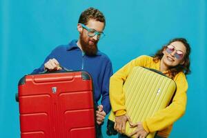 Woman and man smile suitcases in hand with yellow and red suitcase smile fun, on blue background, packing for a trip, family vacation trip. photo