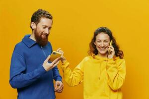 mujer y hombre alegre Pareja con Los telefonos en mano hablando en célula teléfono torcido sonrisa alegre, en amarillo antecedentes. el concepto de real familia relaciones, hablando en el teléfono, trabajo en línea. foto