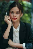 Stylish fashion woman portrait sitting in a cafe at a table and smoking a cigarette releasing smoke from her mouth with red lipstick, a bad habit, a smile with teeth and a thoughtful look photo