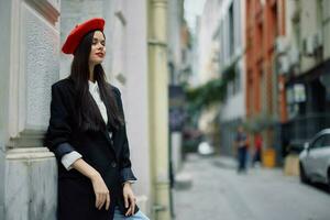 Woman standing near a wall in the city wearing a stylish jacket and red beret with red lips, travel and leisure, French style of dress, spring. photo