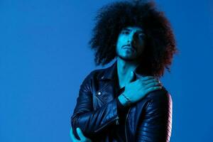 Portrait of fashion man with curly hair on blue background multinational, colored light, black leather jacket trend, modern concept. photo