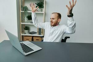 A man in a wheelchair businessman with tattoos in the office behind a laptop, anger and annoyance, hands up, the concept of working a person with disabilities, freedom from social frames photo