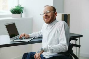 un hombre silla de ruedas, empresario en el oficina trabajando computadora portátil, trabajando en línea, social redes puesta en marcha, integración dentro sociedad, el concepto de trabajando un persona con discapacidades, un real persona de cerca foto