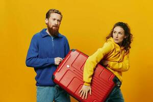 Woman and man smiling, suitcases in hand with yellow and red suitcase smiling merrily and crooked, yellow background, going on a trip, family vacation trip, newlyweds. photo