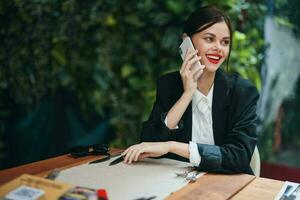 Moda mujer blogger turista en un café con un teléfono en su manos hablando en el teléfono, móvil comunicaciones y el Internet en un primavera viaje, vídeo llamar, Lanza libre trabajo en línea, sonrisa, comunicación foto