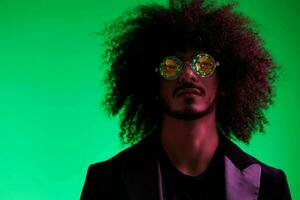 Fashion portrait of a man with curly hair on a green background with sunglasses, multinational, colored pink light, trendy, modern concept. photo