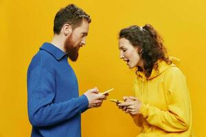 Woman man cheerful couple with phones in hand social networking and communication crooked smile fun and fight, in yellow background. The concept of real family relationships, freelancers, work online. photo