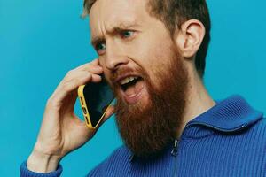 Portrait of a man with a phone in his hands does looking at it and talking on the phone, on a blue background. Communicating online social media, lifestyle photo