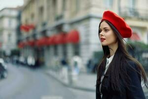 Moda mujer retrato belleza en pie en el calle en frente de el ciudad en elegante ropa con rojo labios y rojo boina, viajar, cinematográfico color, retro Clásico estilo, urbano Moda estilo de vida. foto