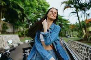 retrato de un mujer morena sonrisa con dientes caminando fuera de en contra un fondo de palma arboles en el zona tropical, verano vacaciones y al aire libre recreación, el despreocupado estilo de vida de un Lanza libre alumno. foto