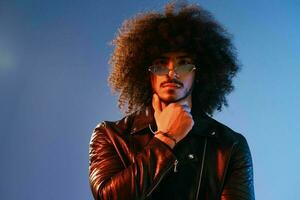 Portrait of a stylish man with curly hair on a blue background multinational, colored light, trendy glasses, modern concept. photo