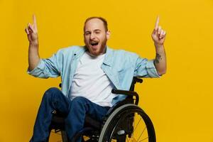 un hombre en un silla de ruedas sonrisa y felicidad, pulgar arriba, con tatuajes en su manos se sienta en un amarillo estudio fondo, el concepto de salud un persona con discapacidades foto