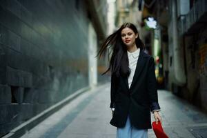 Fashion woman smile with teeth and fun tourist in stylish clothes in jacket and red beret walking down narrow city street flying hair, travel, French style, cinematic color, retro style. photo