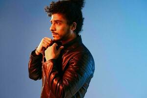 Portrait of a stylish man with curly hair on a blue background multinational, colored light, black leather jacket trend, modern concept. photo