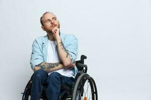 A man in a wheelchair looks at the camera arrogance, with tattoos on his arms sits on a gray studio background, the concept of health is a person with disabilities photo