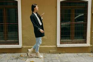 Woman blogger smile with teeth with a phone in her hands walks around the city fashion on the street, spring travel, vacation in the city tourist freelancer, mobile communication and internet for work photo