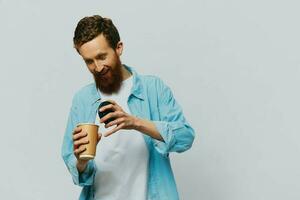 Man hipster with a cup of coffee with a smile on a gray background in a blue shirt and white t-shirt photo