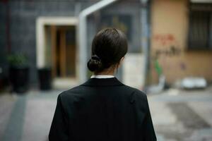 Stylish woman in a black jacket walks along the city street with her back to the camera, follow me photo