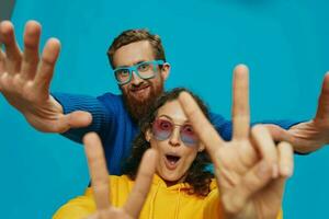 un mujer y un hombre divertido Pareja arrancando y demostración señales con su manos sonriente alegremente, en un azul fondo, el concepto de un real relación en un familia. foto