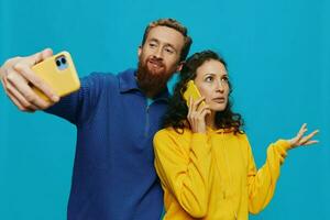 Woman and man funny couple with phones in hand taking selfies crooked smile fun, on blue background. The concept of real family relationships, talking on the phone, work online. photo