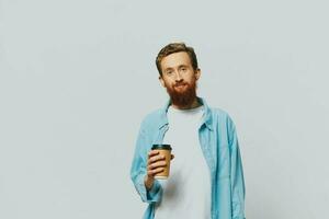 Man hipster with a cup of coffee with a smile on a gray background in a blue shirt and white t-shirt photo