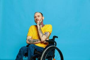 a man sits in a wheelchair thoughtfulness in a t-shirt on a blue background in the studio, the concept of a free barrier-free environment for people with disabilities photo