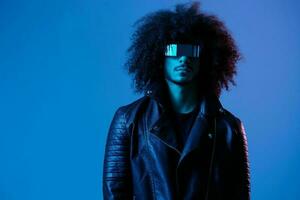 Portrait of fashion man with curly hair with stylish glasses on blue background multinational, colored light, black leather jacket trend, modern concept. photo