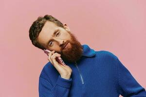 Portrait of a man with a phone in his hands doing looking at it and talking on the phone, on a pink background. Communicating online social media, lifestyle photo