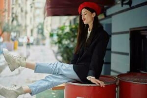 A beautiful woman smiling with teeth stands outside a cafe on a city street, a stylish fashion look of clothes, vacation and travel. photo