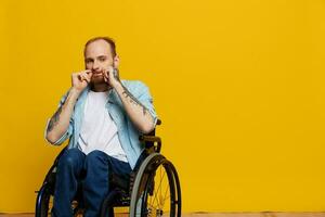 A man in a wheelchair looks at the camera, with tattoos on his arms sits on a yellow studio background, the concept of health is a person with disabilities photo