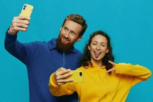 Woman and man funny couple with phones in hand taking selfies crooked smile fun, on blue background. The concept of real family relationships, talking on the phone, work online. photo