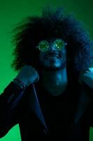 Fashion portrait of a man with curly hair on a green background with sunglasses, multinational, colored pink light, trendy, modern concept. photo