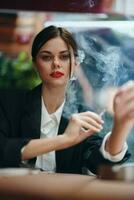 elegante mujer se sienta en un café a un mesa y fuma un cigarrillo, un malo hábito foto