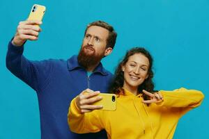 Woman and man funny couple with phones in hand taking selfies crooked smile fun, on blue background. The concept of real family relationships, talking on the phone, work online. photo