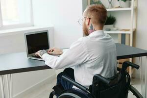 man wheelchair businessman with tattoos in the office works at a laptop online, business process from the back, copy space, integration into society, the concept of working a person with disabilities photo